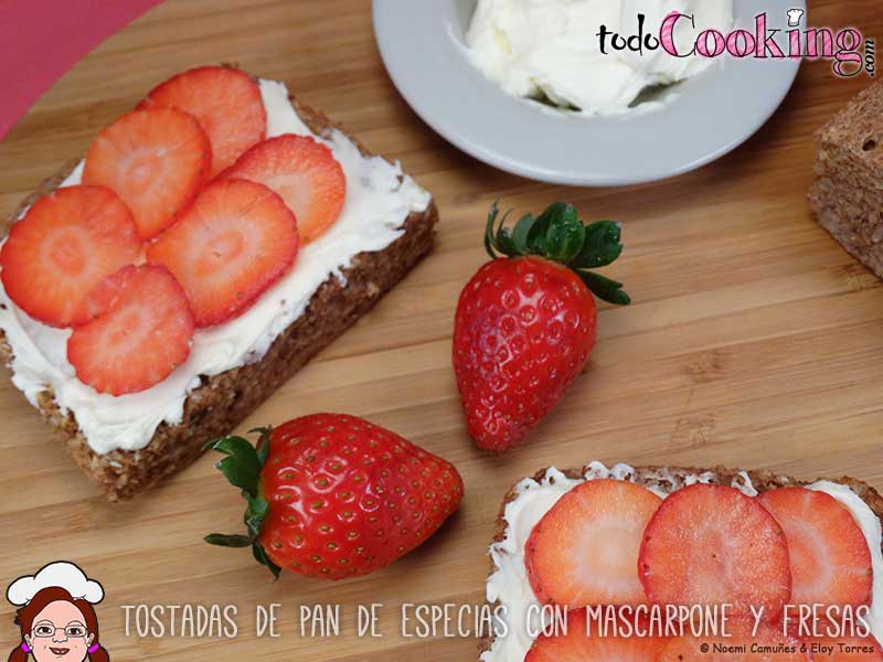 Vista cenital de las tostadas de pan de especias untadas con queso mascarpone y fresas, en el centro unas fresas para decorar.