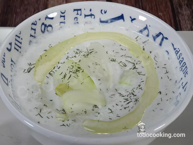 Plano detalle de sopa fría de pepino cremosa con eneldo picado, decorada con láminas de pepino y un hilo de aceite de oliva.